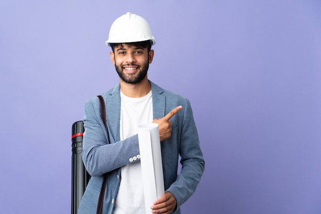 Jovem arquiteto marroquino com capacete segurando plantas apontando para o lado para apresentar um produto