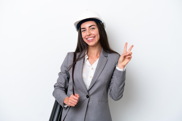 Jovem arquiteto mulher caucasiana com capacete e segurando plantas isoladas no fundo branco sorrindo e mostrando sinal de vitória