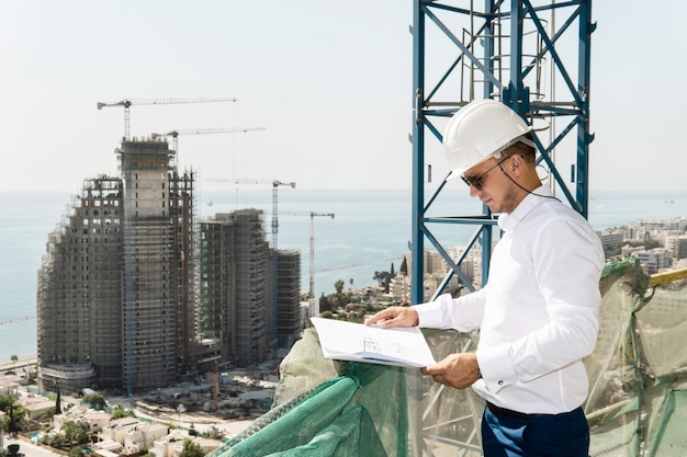 Foto jovem arquiteto ou empresário confiante usando capacete com um bluepritns em uma construção perto do mar azul