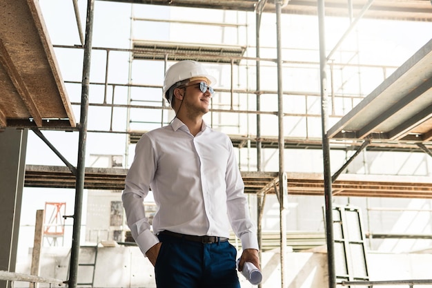 Foto jovem arquiteto ou empresário usando capacete e segurando plantas em um canteiro de obras