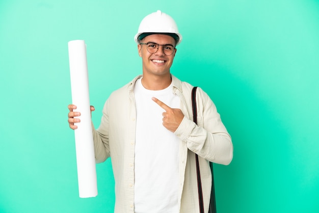 Jovem arquiteto segurando plantas sobre um fundo isolado apontando para o lado para apresentar um produto