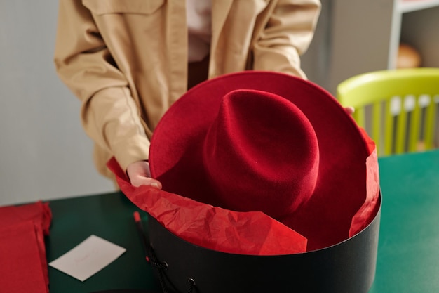 Jovem artesã colocando novo chapéu panamá de feltro carmesim em caixa redonda preta