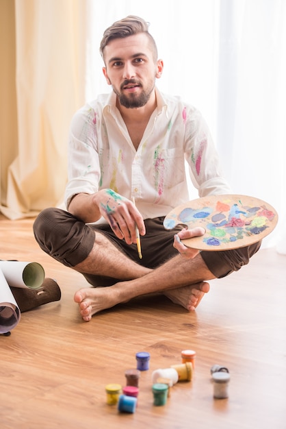 Jovem artista está no chão com tintas.