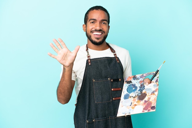 Jovem artista latino segurando uma paleta isolada em um fundo azul, contando cinco com os dedos