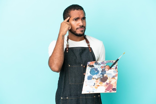 Jovem artista latino segurando uma paleta isolada em um fundo azul, tendo dúvidas e pensando