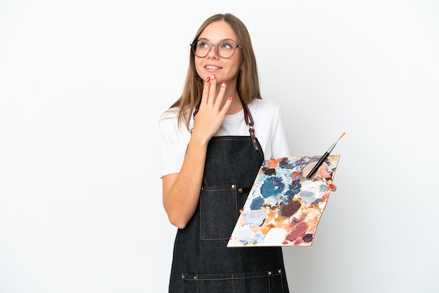 Jovem artista lituana segurando uma paleta isolada em fundo branco olhando para cima enquanto sorria