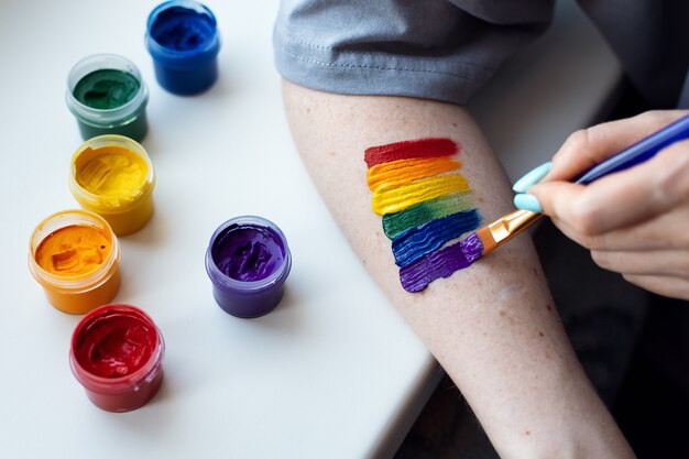 Jovem artista pinta um sinal de comunidade LGBT multicolorido no braço