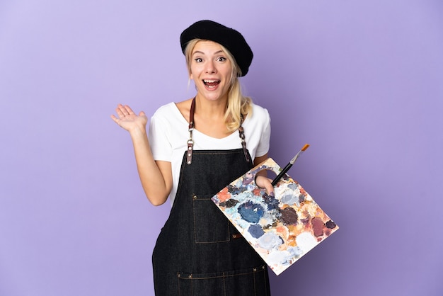 Jovem artista russa segurando uma paleta isolada em um fundo roxo com expressão facial chocada