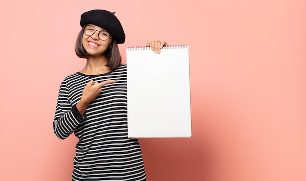 Jovem artista sorrindo alegremente, sentindo-se feliz e apontando para os lados e para cima, mostrando o objeto no espaço da cópia