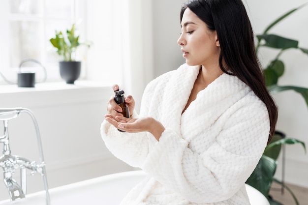 Jovem asiática a bombear produto de beleza na palma da mão.