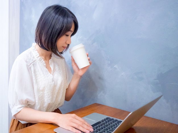 Jovem asiática bebendo na frente de um laptop