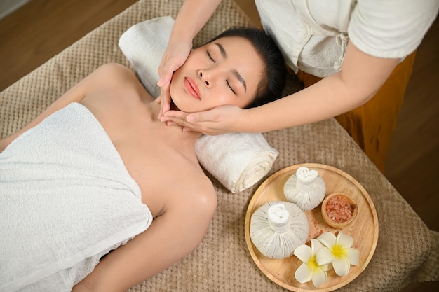 Jovem asiática calma e relaxada com massagem facial ou tratamento facial no salão de spa de beleza