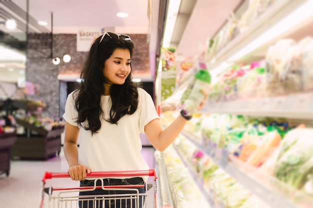 Jovem asiática com carrinho de compras no conceito de compras de supermercado