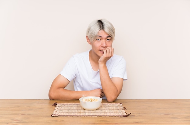 Jovem asiática com ramen em uma mesa nervosa e assustada