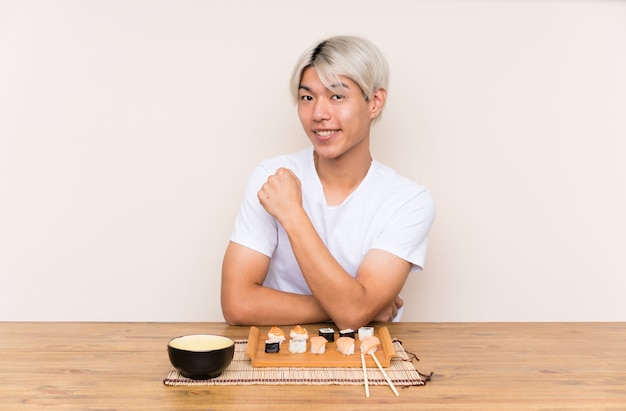 Jovem asiática com sushi em uma mesa comemorando uma vitória