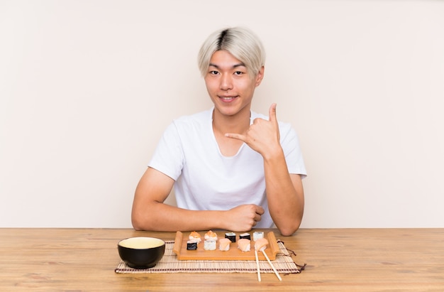Jovem asiática com sushi em uma mesa fazendo gesto de telefone
