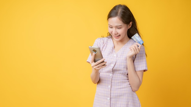 Jovem asiática de vestido rosa segurando telefone em fundo amarelo