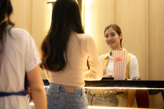 Jovem asiática em fila para comprar bilhetes de cinema e com pipocas na mão e bebida