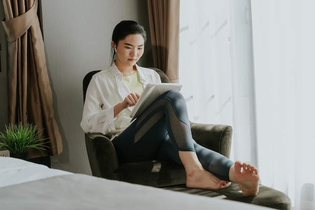 Jovem asiática em roupas casuais fáceis usando tablet digital ouvindo música relaxante em casa