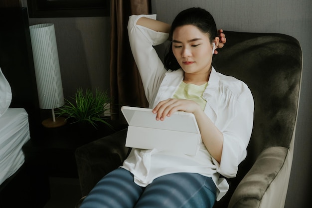 Jovem asiática em roupas casuais fáceis usando tablet digital ouvindo música relaxante em casa