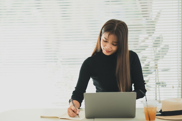 Jovem asiática em roupas casuais inteligentes trabalhando no laptop enquanto está sentada no escritório criativo ou no café jovem trabalhando com o laptop na mesa de madeira no café