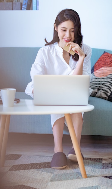 Jovem asiática fazendo compras online com cartão de crédito e laptop em casa