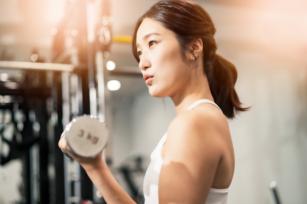 Jovem asiática fazendo treinamento muscular com halteres