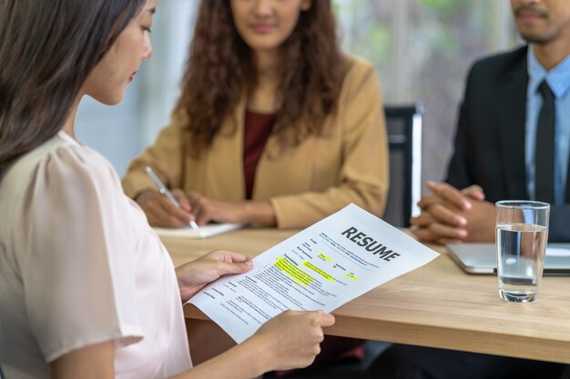 Foto jovem asiática formada segurando o documento de currículo e se preparando para dois gestores