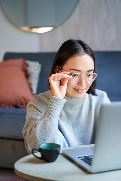 Foto jovem asiática freelancer profissional sentada na sala de estar e trabalhando com computador estudando um