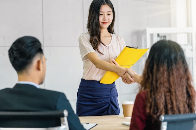 Jovem asiática graduada apertando a mão com dois gerentes para dar as boas-vindas antes do início da entrevista de emprego