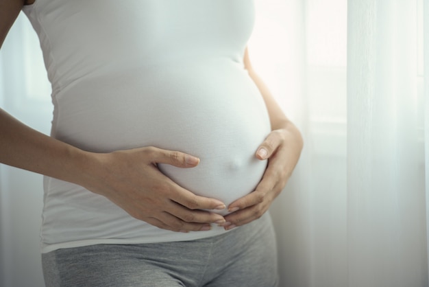 Jovem asiática grávida com as mãos na barriga