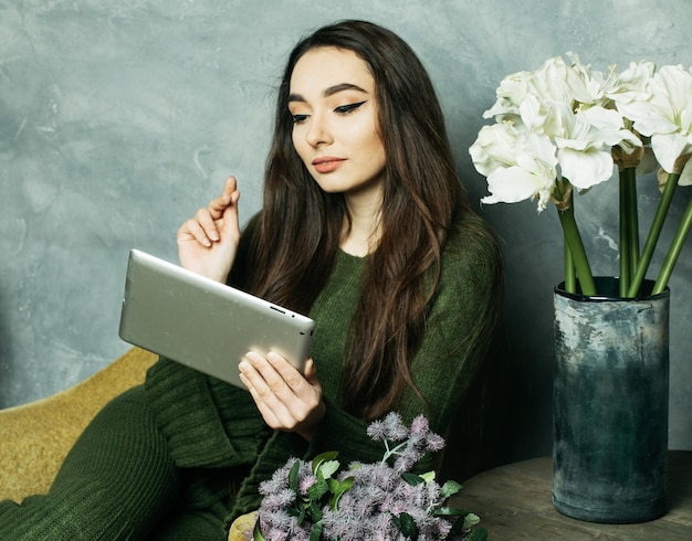 Jovem asiática malha com um tablet se senta em uma cadeira ao lado de um buquê de flores