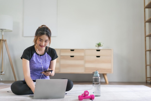 Jovem asiática ouvindo música e assistindo vídeo de fitness para se preparar para fazer exercícios em casa