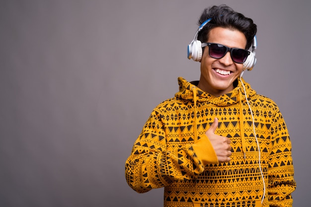 jovem asiática ouvindo música enquanto usava capuz contra parede cinza