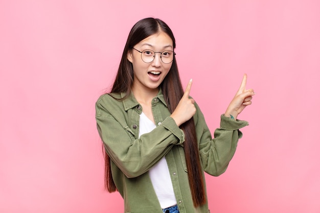 Jovem asiática se sentindo alegre e surpresa, sorrindo com uma expressão chocada e apontando para o lado