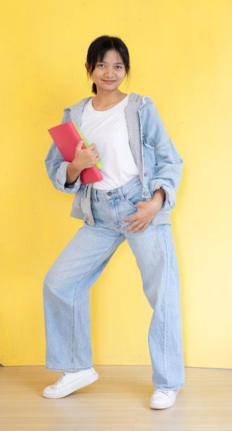 Foto jovem asiática segura livro rosa em fundo amarelo