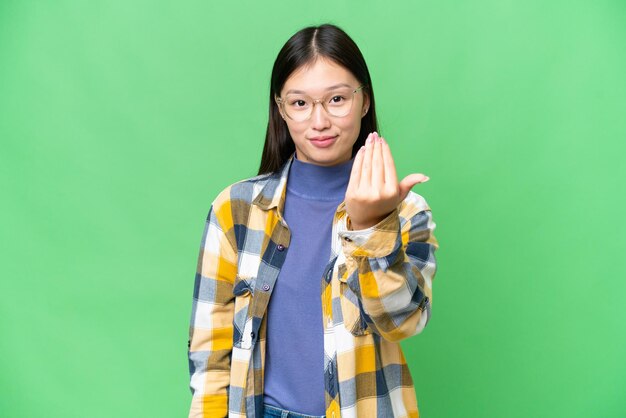 Jovem asiática sobre fundo croma isolado convidando para vir com a mão Feliz por você ter vindo