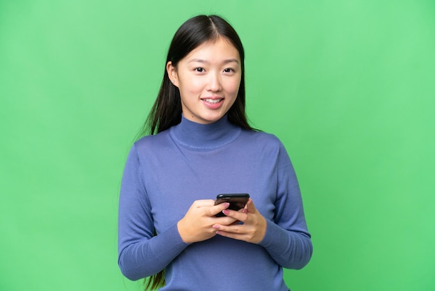 Jovem asiática sobre fundo croma isolado enviando uma mensagem com o celular