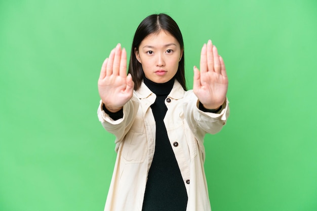 Jovem asiática sobre fundo croma isolado fazendo gesto de parada e decepcionada