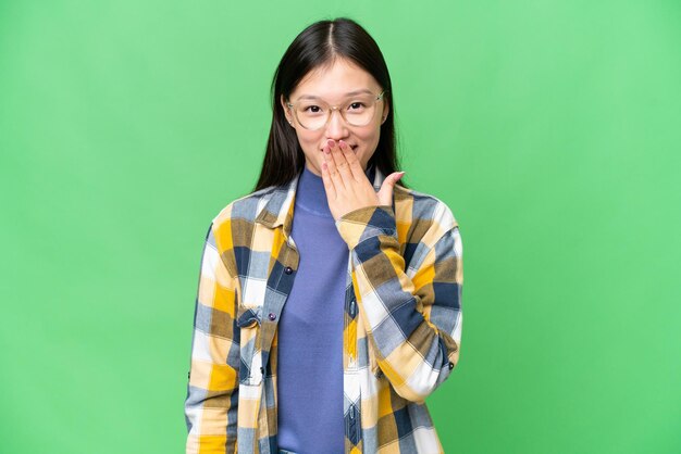 Jovem asiática sobre fundo croma isolado feliz e sorridente cobrindo a boca com a mão