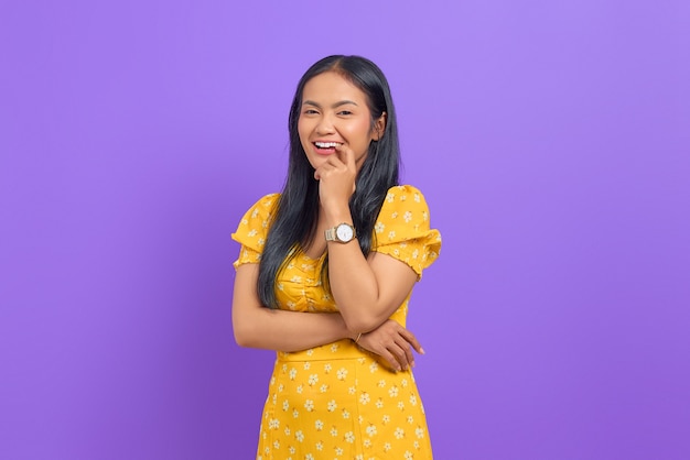 Jovem asiática sorridente usando um vestido amarelo e parecendo confiante em um fundo roxo