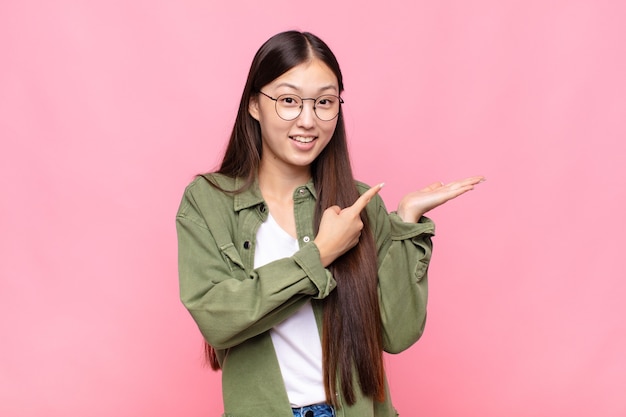 Jovem asiática sorrindo alegremente e apontando para copiar o espaço na palma da mão ao lado, mostrando ou apresentando um objeto