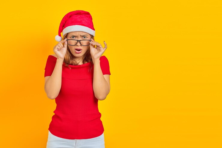 Foto jovem asiática surpresa usando chapéu de natal com óculos, enquanto a boca aberta sobre fundo amarelo