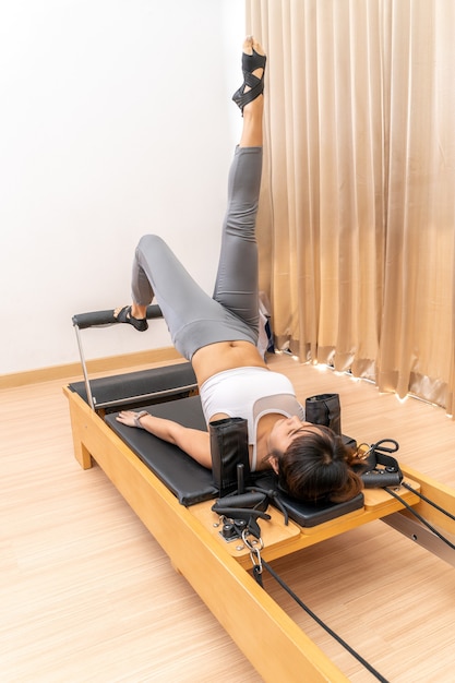 Foto jovem asiática trabalhando em uma máquina reformadora de pilates durante seu treinamento de exercícios de saúde