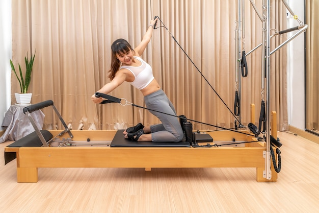 Foto jovem asiática trabalhando em uma máquina reformadora de pilates durante seu treinamento de exercícios de saúde