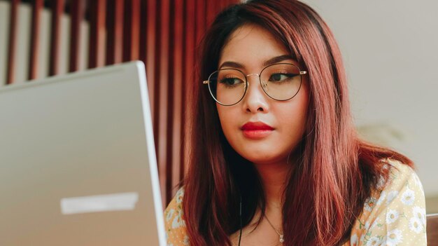 Jovem asiática trabalhando no laptop enquanto está sentada no café olhando documentos