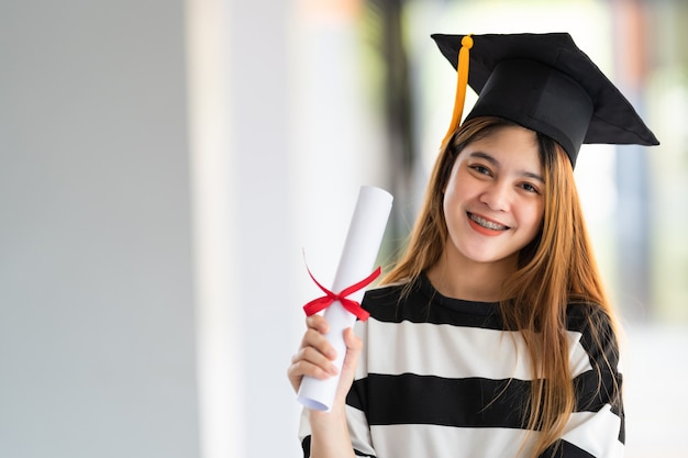 Jovem asiática, universitária, com vestido de formatura e cartolina, possui um certificado de graduação