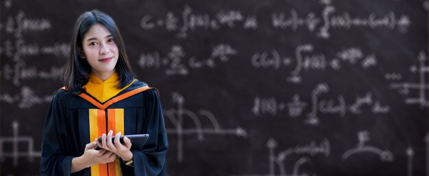 Jovem asiática, universitária, com vestido de formatura e cartolina, possui um certificado de graduação