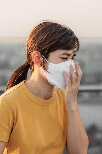 Jovem asiática usando máscara respiratória n95 protege e filtra pm25 ou material particulado contra poluição do ar ruim na cidade índice de qualidade do ar aqi conceito de saúde insalubre