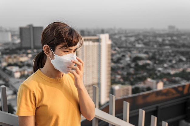 Jovem asiática usando máscara respiratória N95 protege e filtra pm25 ou material particulado contra poluição do ar ruim na cidade Índice de qualidade do ar AQI Conceito de saúde insalubre